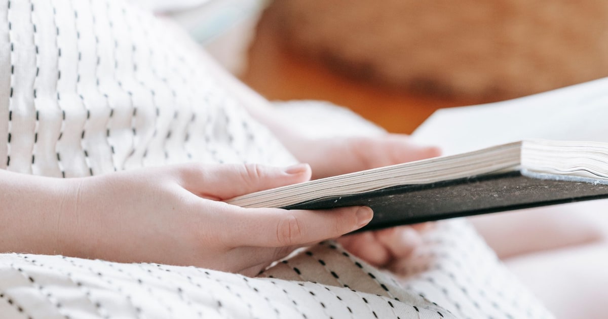 A person reading a printed book at home in warm sunlight.