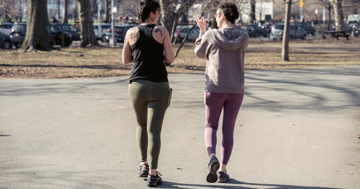 Two women walking together along a sunlit park path.